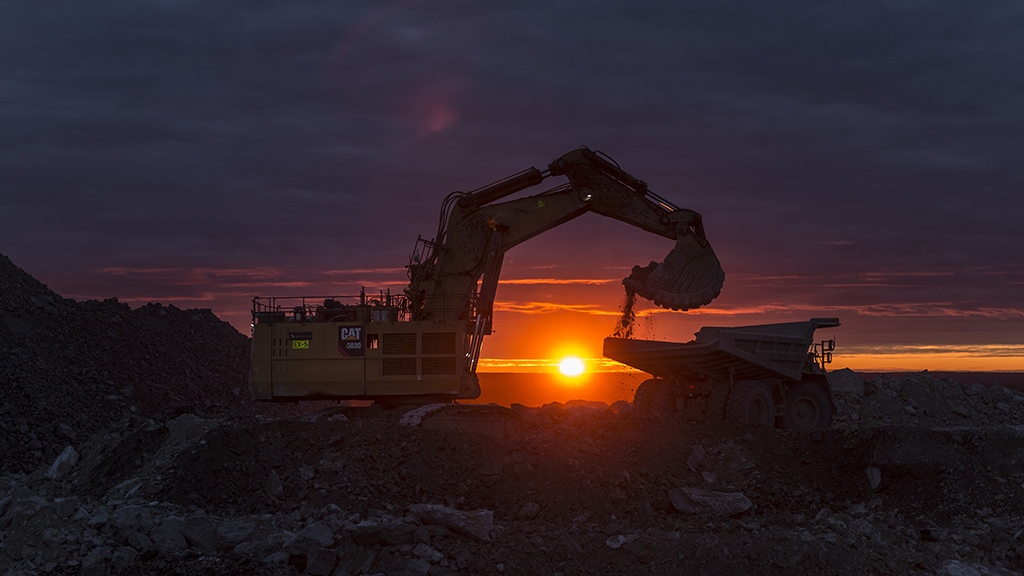 Bulldozer dropping dirt into a truck at sunrise