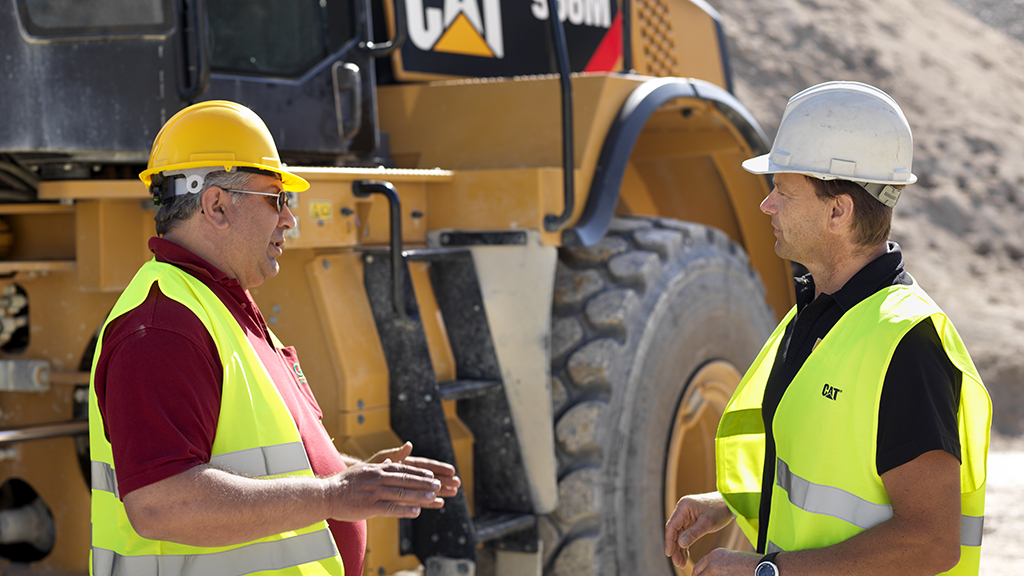Two construction workers talking in front of a cat machine 